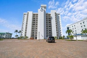 A multi-story hotel with a prominent 'S' logo on the facade, a paved courtyard, and palm trees. - Sunset 304-Charming Beachfront Condo with Gulf Views (Fort Myers Beach)