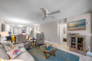 Ein modernes Wohnzimmer mit Deckenventilator, einer Couch, einem Couchtisch und einem Bücherregal.