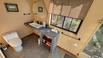 A bathroom with a toilet, sink, mirror, and window.