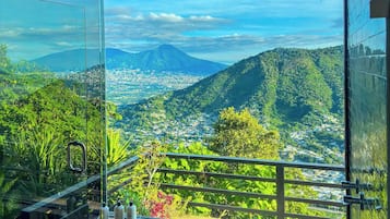A balcony with a glass door overlooking a cityscape and mountains.
