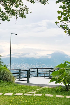 A park with a paved walkway, benches, and a view of a city and mountains in the distance. - The Monticello Cave (Los Planes de Renderos)