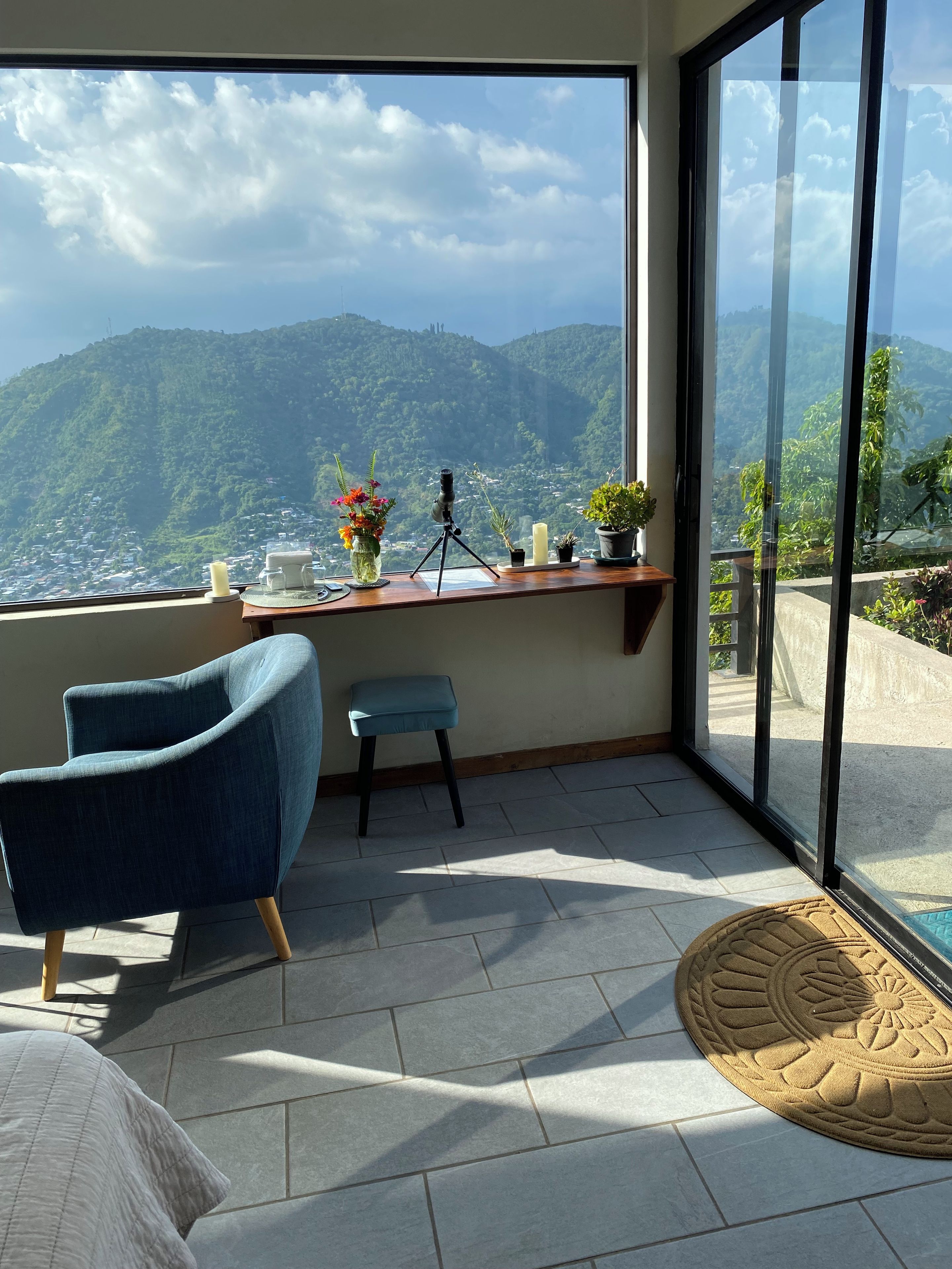 Une pièce avec vue sur les montagnes, un bureau avec un appareil photo posé sur un trépied, une chaise et un petit tabouret.