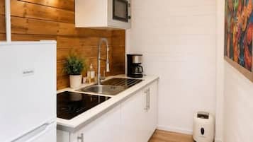 Una cocina compacta con muebles blancos, un microondas integrado y piso de madera.