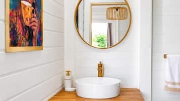 Un baño con lavamanos blanco, encimera de madera, espejo redondo y una alfombra mullida blanca.