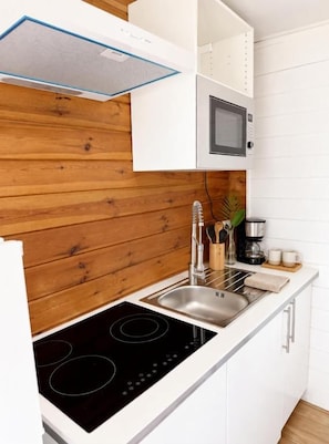 Una cocina con encimera blanca, placa de inducción negra, fregadero de acero inoxidable y microondas.