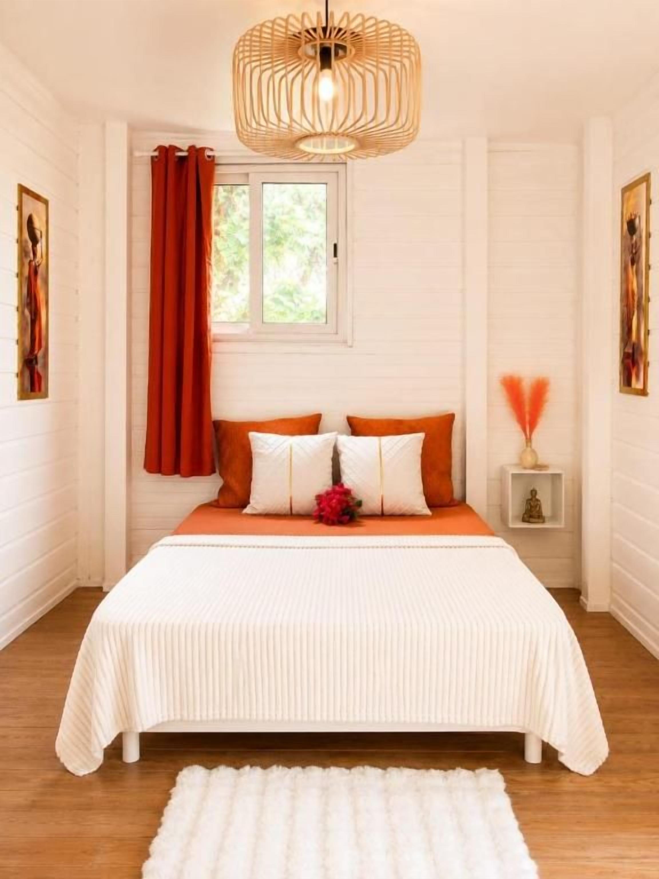 Un dormitorio con cama, una ventana con cortinas, una mesita de noche con lámpara y una obra de arte colgada en la pared.