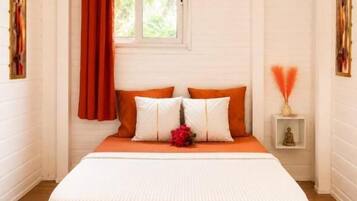 Un dormitorio con cama, una ventana con cortinas, una mesita de noche con lámpara y una obra de arte colgada en la pared.