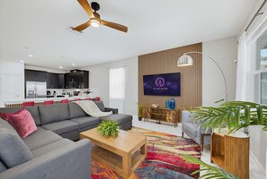 A modern living room with a sofa, coffee table, and a flat-screen TV mounted on a wall. - 9BR | Star Wars & Toy Story | Pool + Arcade (Four Corners)
