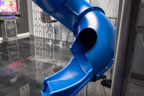 A blue slide structure in a room with a polished floor, a Star Wars themed display, and a bar area with glasses. - 9BR | Star Wars & Toy Story | Pool + Arcade (Four Corners)
