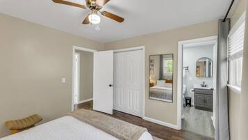 A bedroom with a bed, a ceiling fan, a door leading to a bathroom, and a window with curtains.