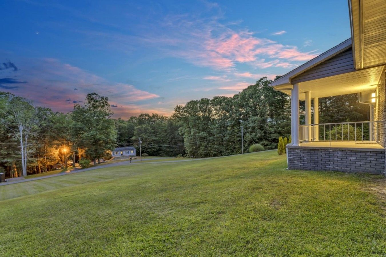 A well-maintained lawn with a house featuring a covered porch and a brick foundation.