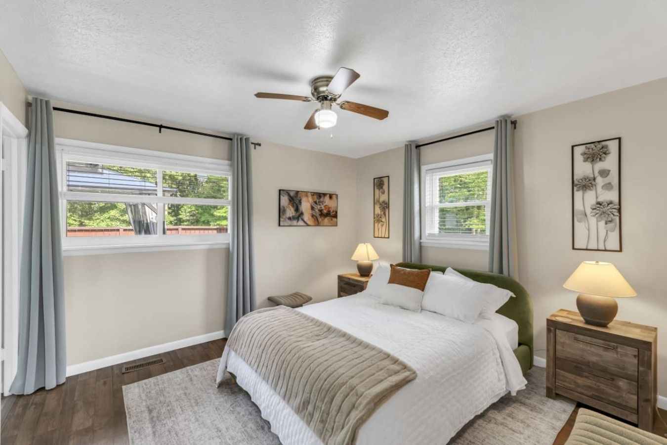 A bedroom with a bed, two bedside tables, a ceiling fan, and two windows with curtains.