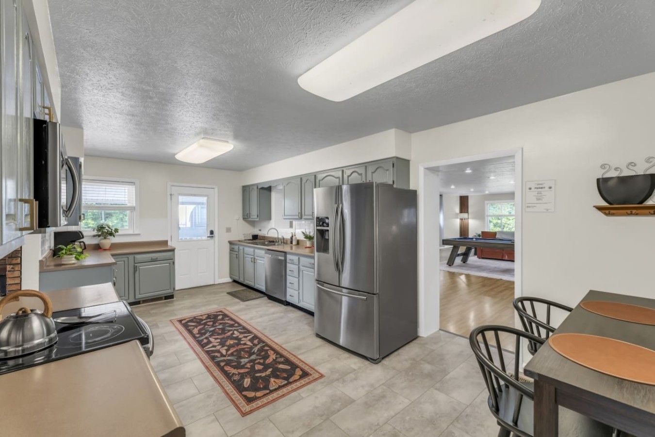 A modern kitchen with stainless steel appliances, grey cabinetry, and a dining area with a wooden table and chairs.