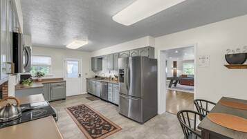 A modern kitchen with stainless steel appliances, grey cabinetry, and a dining area with a wooden table and chairs.