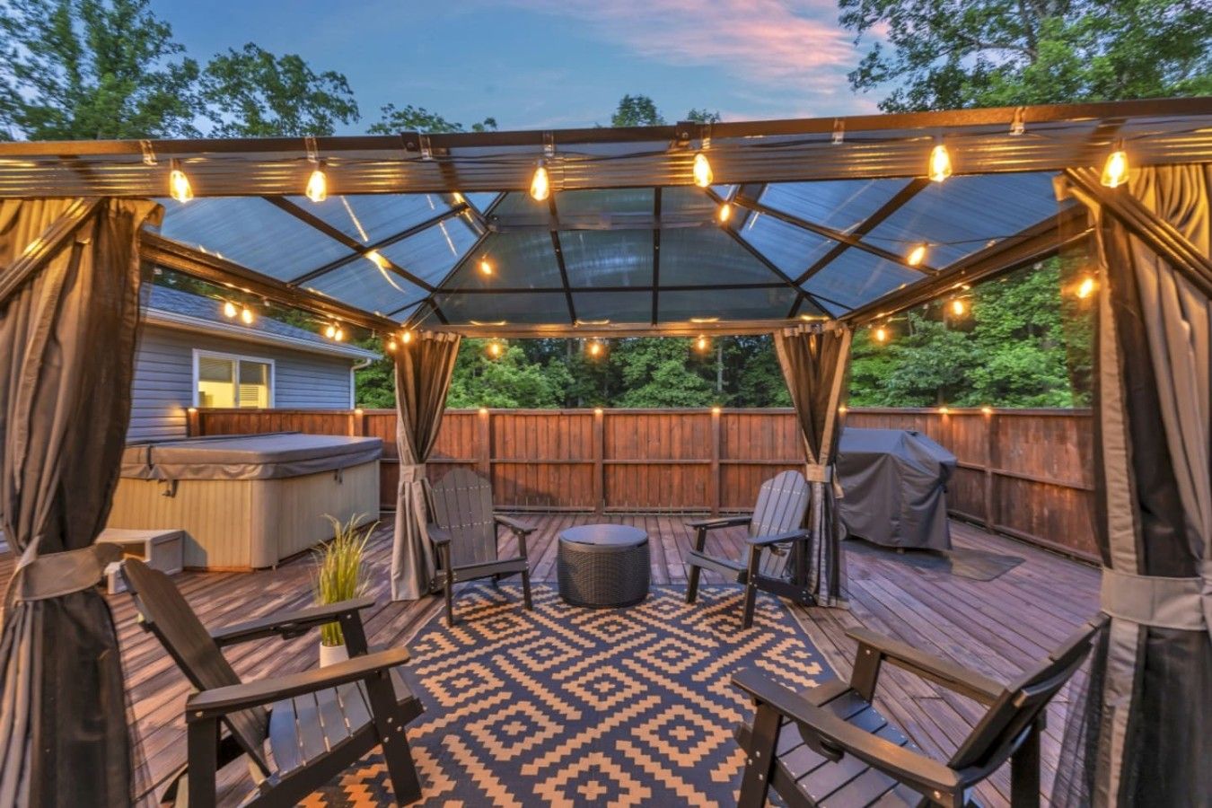 A covered outdoor patio with a glass ceiling, string lights, and outdoor furniture.