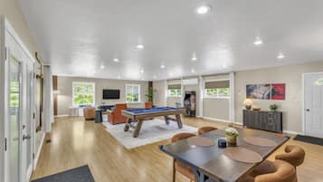 Un vaste espace de vie comprenant une table de billard, une table à manger avec des chaises et un téléviseur à écran plat fixé au mur.