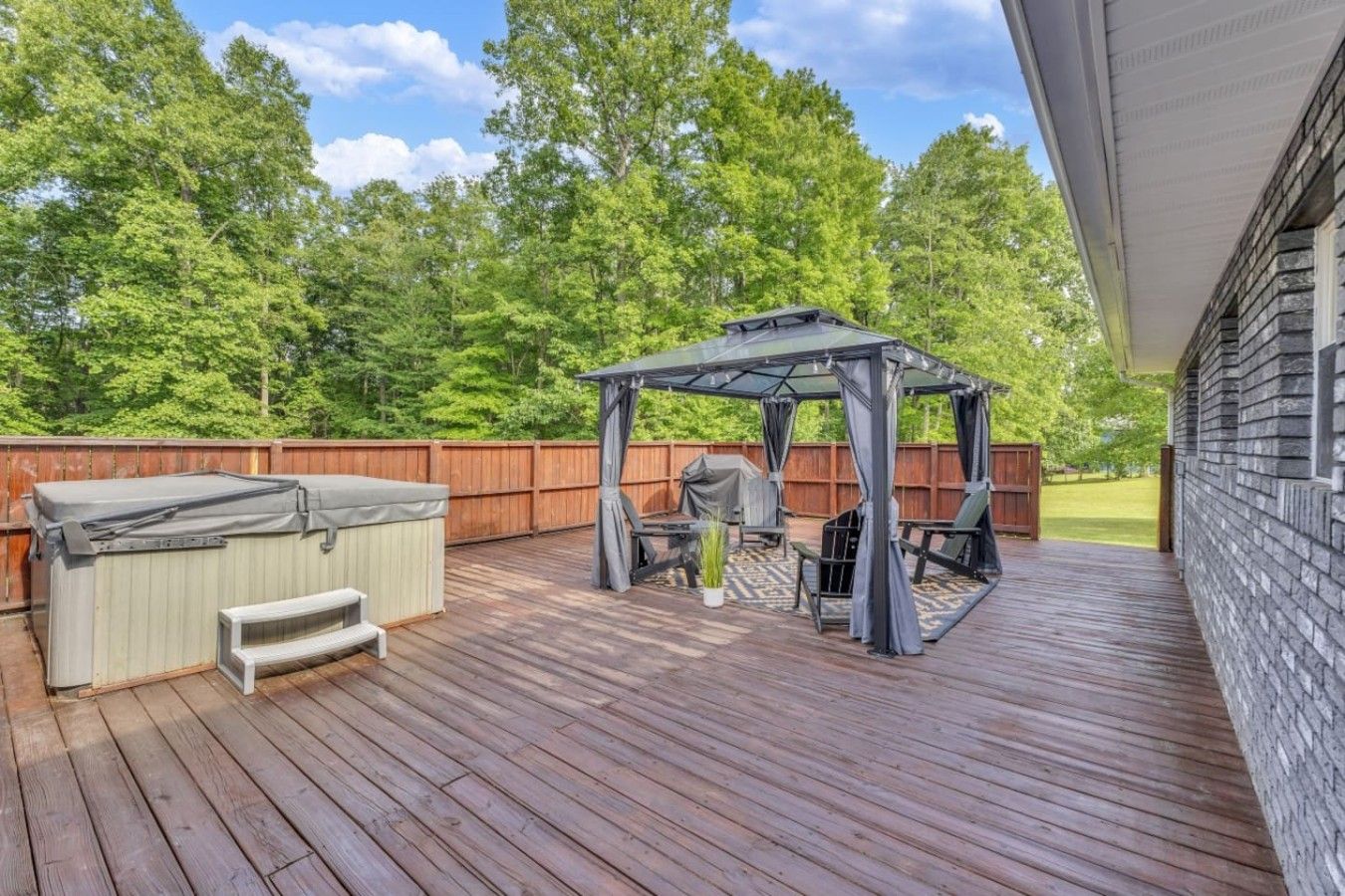 Une terrasse en bois avec un jacuzzi, un espace salon couvert et un barbecue.