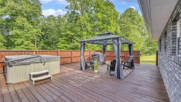 Une terrasse en bois avec un jacuzzi, un espace salon couvert et un barbecue.