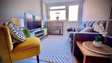 Una sala de estar con un sofá, un sillón amarillo, un televisor, una mesa de centro y un ventanal con vistas.