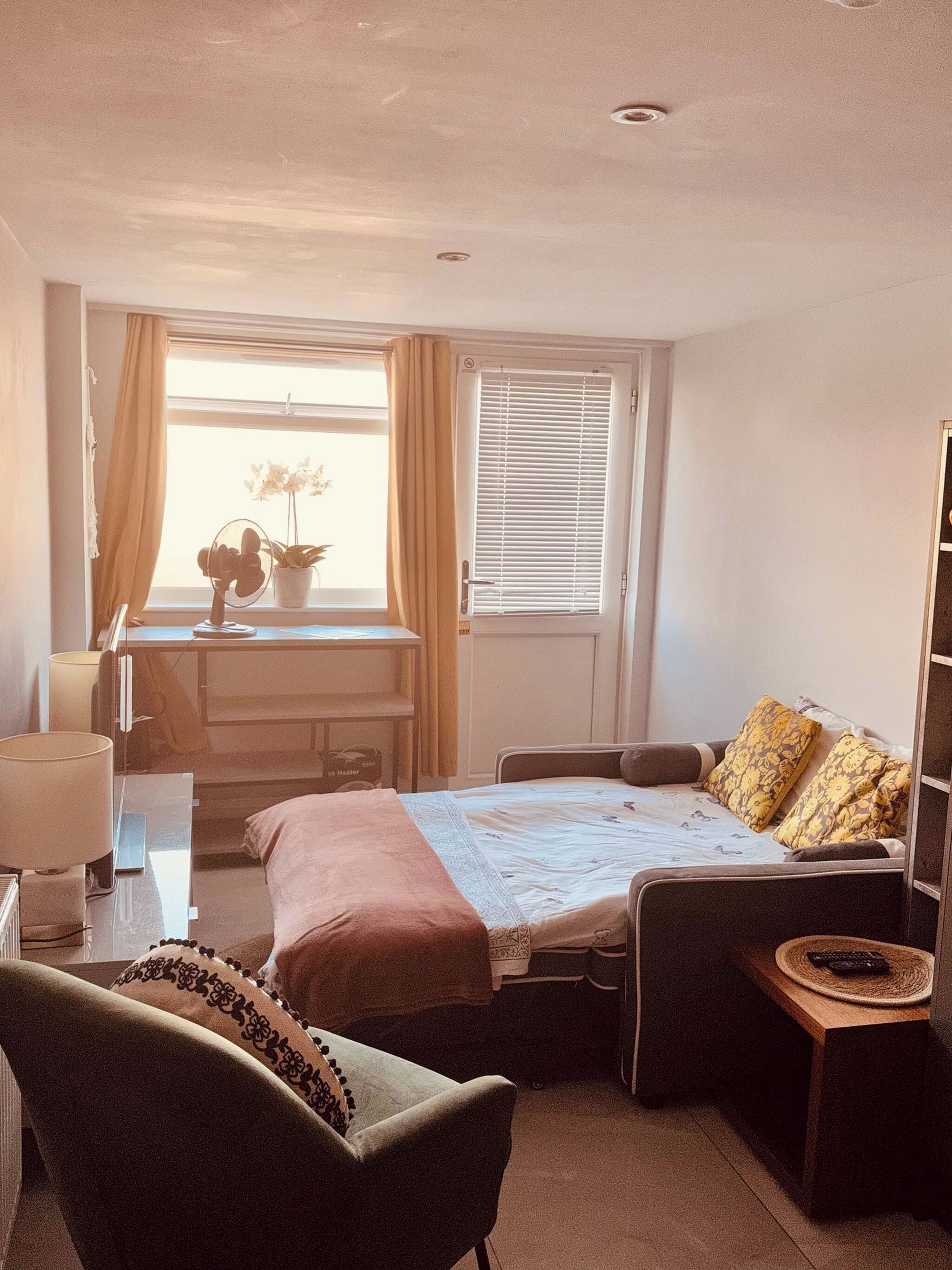 A compact hotel room with a bed, a chair, a desk, and a window with curtains.