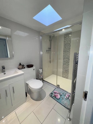 A modern bathroom with a glass shower enclosure, a white toilet, and a vanity with a mirror. - Shal Inn at Heathrow Free Parking and Ride on Request (Slough)
