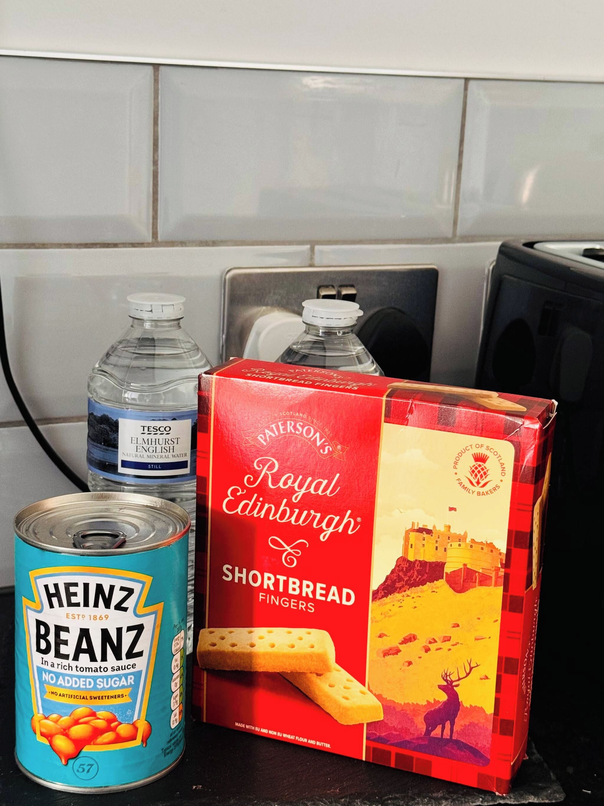 A kitchen counter with a can of Heinz Beanz, a bottle of water, and a box of Paterson's Edinburgh Shortbread Fingers.