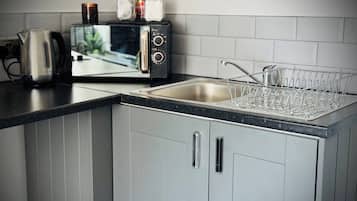 Una cocina con microondas integrado, hervidor y escurreplatos.