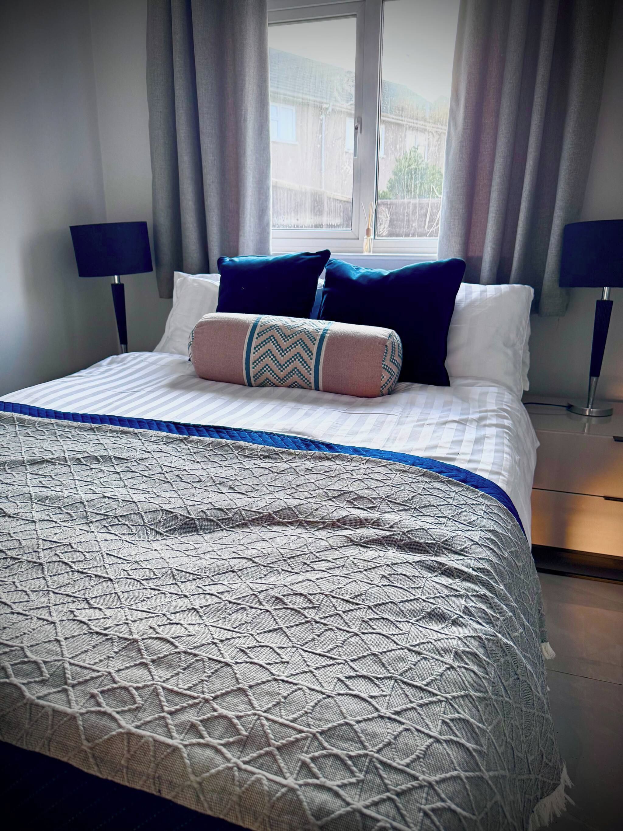 A neatly made bed with a patterned bedspread, pillows, and a bedside lamp.