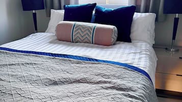 A neatly made bed with a patterned bedspread, pillows, and a bedside lamp.
