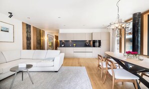 A modern living room with a white sofa, a dining table with chairs, and a kitchen in the background. - A MODERN ALPINE STYLE APARTMENT WITH  BREATHTAKING DIRECT VIEW OF THE MATTERHORN (Zermatt)