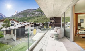 A modern balcony with a glass railing, a seating area with a sofa and chairs, and a view of a mountainous landscape. - A MODERN ALPINE STYLE APARTMENT WITH  BREATHTAKING DIRECT VIEW OF THE MATTERHORN (Zermatt)