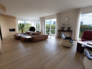 A modern living room with a sectional sofa, a round black chair, and a dining area with a table and chairs. - Le Rooftop Eiffel & La Défense - Welkeys (Neuilly-sur-Seine)