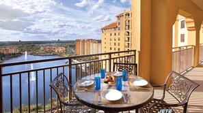 A balcony with a table set for dining, overlooking a body of water and buildings. - 1BR DELUXE sleeps 4- Holiday Get Away 5min to Disney-Wyndham Bonnet Creek Resort (Lake Buena Vista)