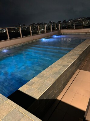 A rectangular indoor swimming pool with a tiled edge, surrounded by a balcony with a railing. - Elegant studio with a beautiful view. (Porto Alegre)