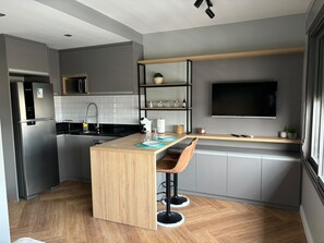 Eine moderne Küche mit einer zentralen Kochinsel, Barhocker, einer Mikrowelle und einem an der Wand befestigten Flachbildfernseher.