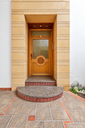 Une porte en bois dotée d’un panneau de verre et d’un emblème circulaire décoratif, qui donne sur un hall d’entrée carrelé de pierres avec une bordure ornée.