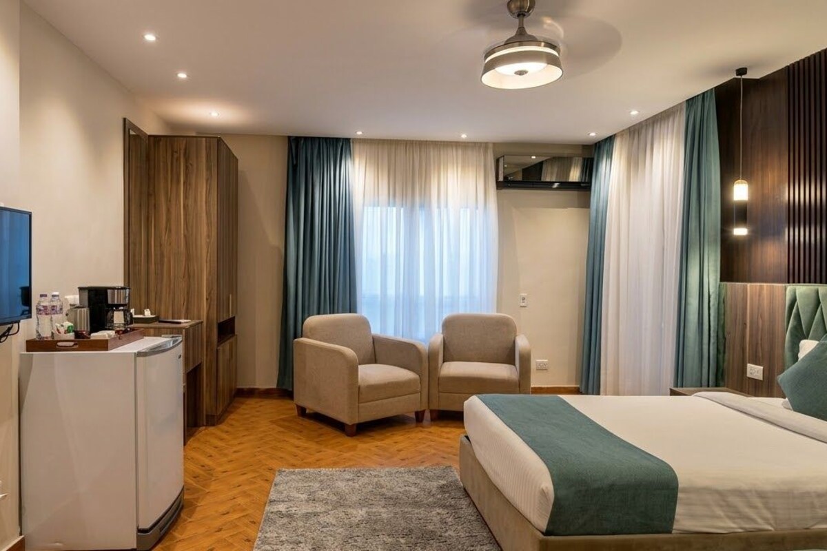 A hotel room with a bed, a desk with a television, a chair, and a window with curtains.