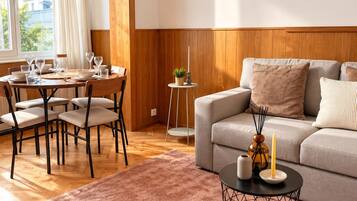 Una sala de estar moderna con comedor, paneles de madera, un sofá gris y una mesa de centro con velas.