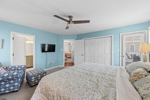 Ein Schlafzimmer mit einem Bett, einem Deckenventilator, einem Fernseher und einer Tür zu einem anderen Raum.