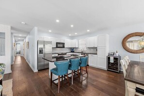 A modern kitchen with white cabinets, a central island, bar stools, and a wine rack. - Near Beach 4BR OCNJ Retreat / Rooftop Deck & Garage (Ocean City)