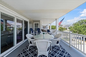 A covered porch with a table and chairs, an American flag, and a view of a residential area. - Near Beach 4BR OCNJ Retreat / Rooftop Deck & Garage (Ocean City)