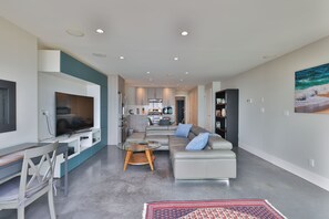 A modern living room with a sofa, a glass coffee table, and a flat-screen TV. - The Beachcomber Suite (Victoria)