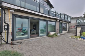 A modern two-story house with large sliding glass doors, a covered patio, and a visible garage. - The Beachcomber Suite (Victoria)