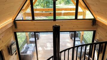 Een houten interieur met een balkon, een trap en een zithoek met kussens.