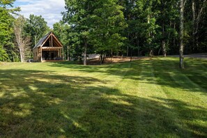 A wooden cabin with a porch, surrounded by a grassy field and dense trees. - Glimmerwood Grove - Modern Cabin (Nassau)