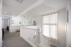 Un intérieur spacieux avec un plafond haut, un escalier doté de rampes blanches et de grandes fenêtres ornées de rideaux légers.