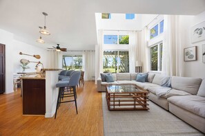 A spacious living area with a large sofa, a coffee table, and a kitchen area with a bar. - Desirable Villa Walk 2 beach Light & Bright Heated Pool (Waikoloa Village)