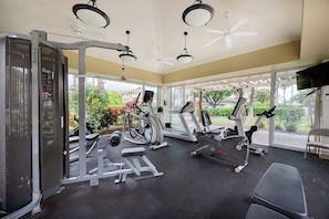 Ein Fitnessstudio mit unterschiedlichen Trainingsgeräten, großen Fenstern und einem Deckenventilator.