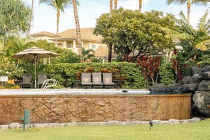 A pool area with a stone wall, lounge chairs, and a sign. - Desirable Villa Walk 2 beach Light & Bright Heated Pool (Waikoloa Village)