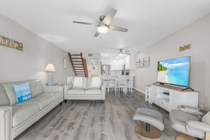 A modern living room with a sofa, a coffee table, a TV, and a dining area with chairs and a table. - Coastal Bokeelia Getaway at Bocilla Island Club! (Bokeelia)